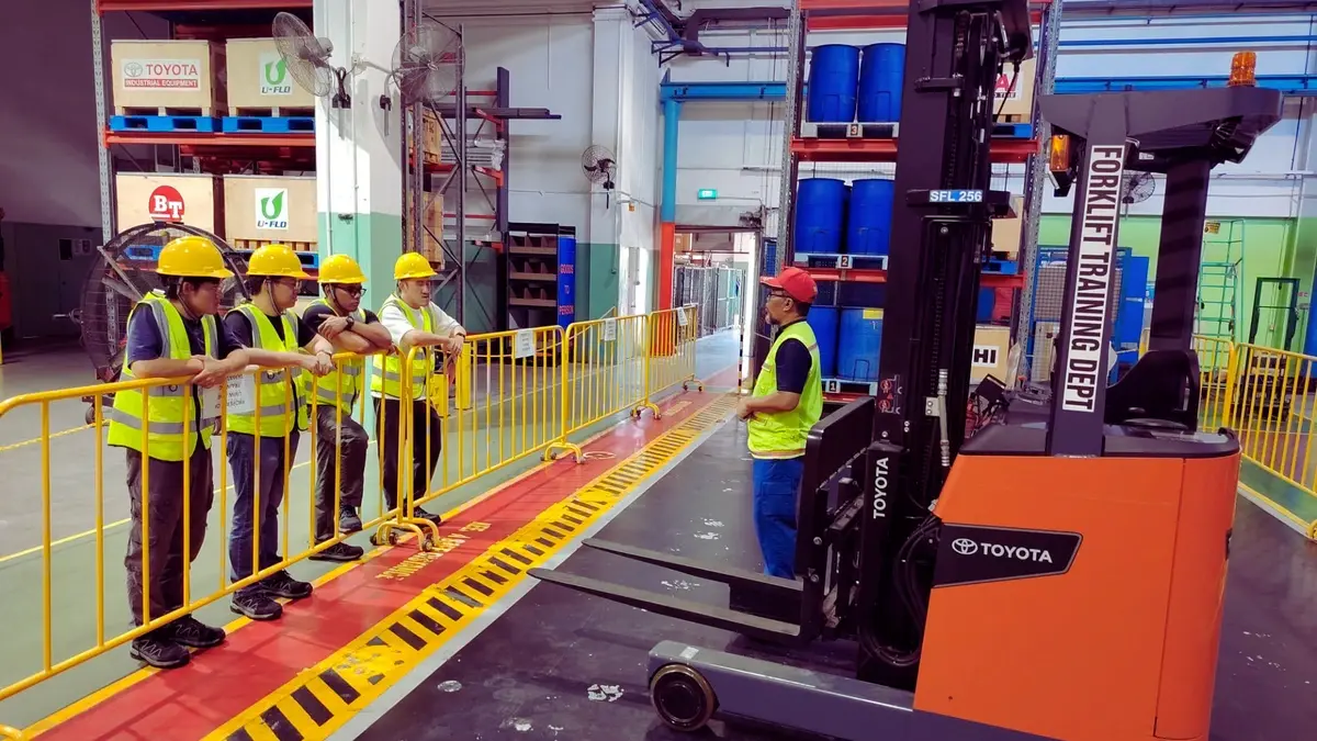 Forklift training practice in Singapore with trainees learning safe forklift operation in a warehouse setting.