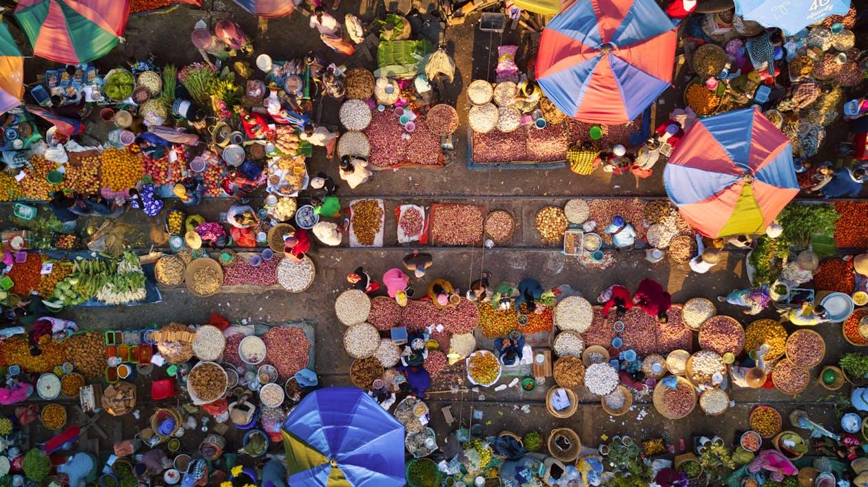 Free Colorful outdoor market bustling with people, fruits, and vegetables viewed from above. Stock Photo