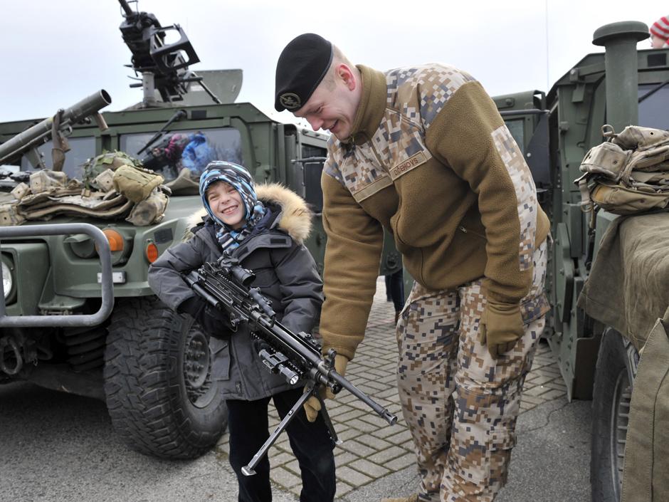 A Latvian Army troop member shows his gun to a young  boy, during the ''Dragoon Ride'' military exercise, in Riga, Latvia, Sunday, March 22, 2015. The troops began the trek on March 21, and will travel through Latvia, The Czech Republic and onto Germany by April 1 in an exercise designed to reinforce America's allies. (AP Photo/Oksana Dzadan)