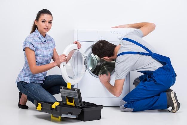 Repairman is repairing a washing machine for housewife.