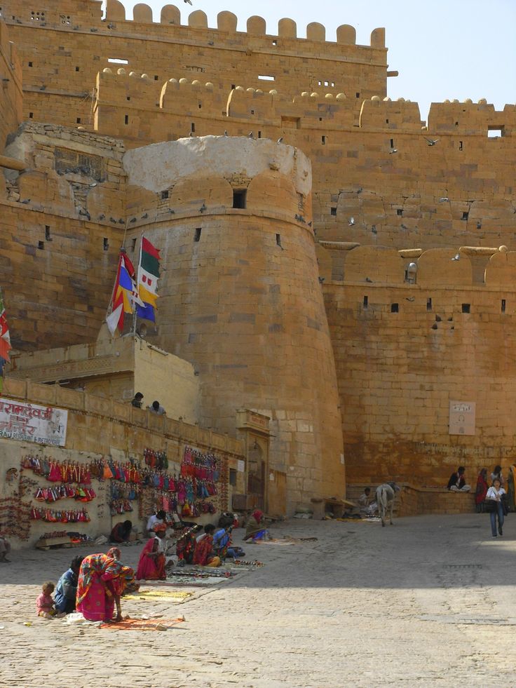 This may contain: people are sitting on the ground in front of an old castle like structure with flags flying from it