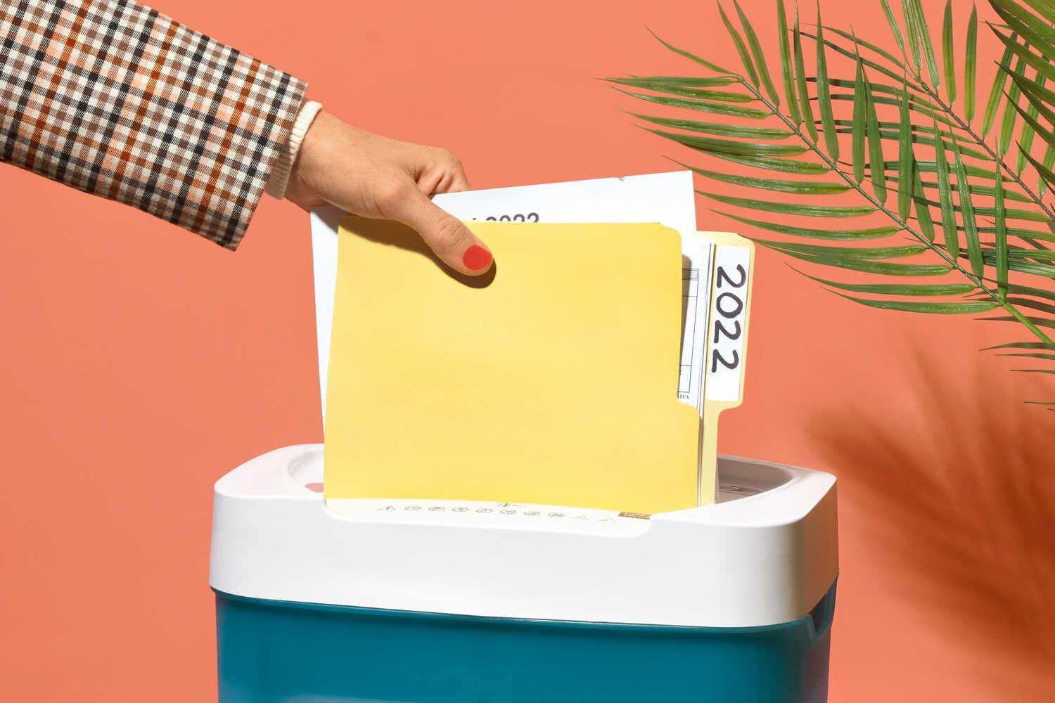 A woman’s hand feeds a folder labeled 2022 into a paper shredder.