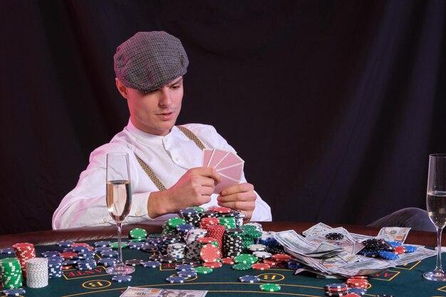 Photo man playing poker at casino sitting at table with stacks of chips money champagne cards black backgr
