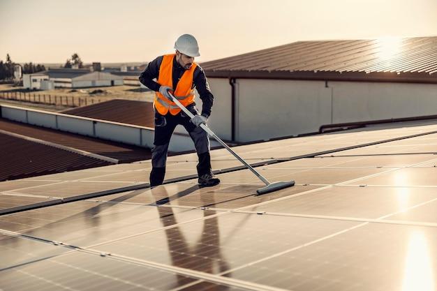 Photo a worker brooming solar panels on the roof at sunset
