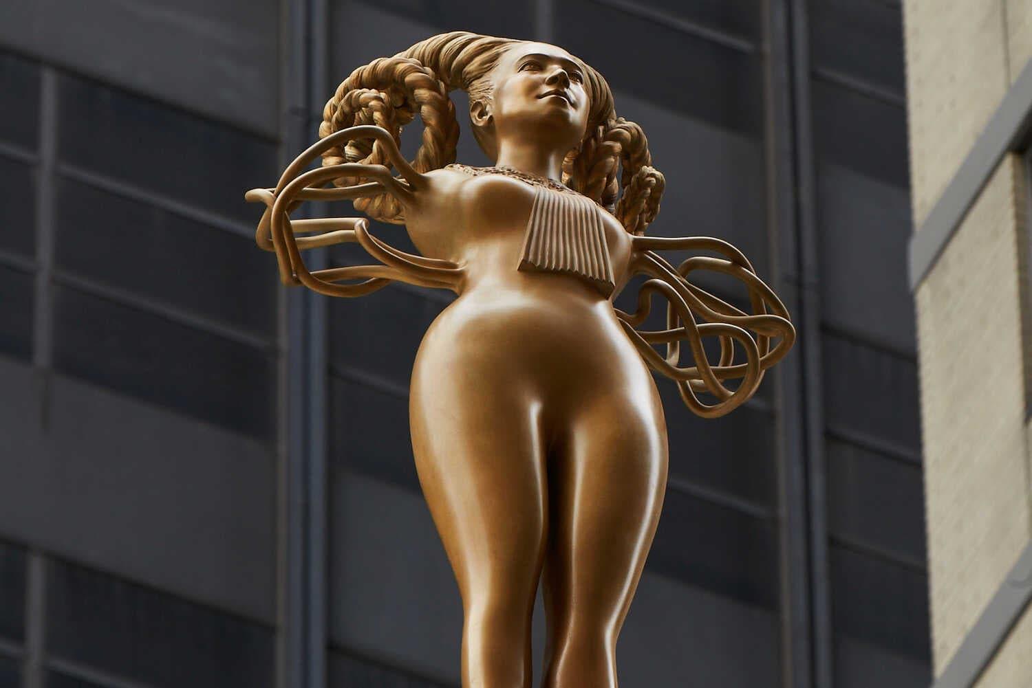 A golden eight-foot female sculpture, emerging from a pink lotus flower near Madison Square Park, wears Justice Ruth Bader Ginsburg’s signature lace collar.