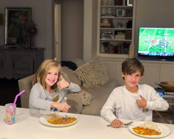 girl and boy eating lamb curry with football game on tv
