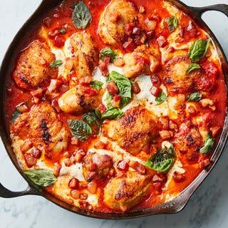 A cast-iron skillet full of chicken, red sauce and cheese, and topped with herbs, is photographed from overhead.