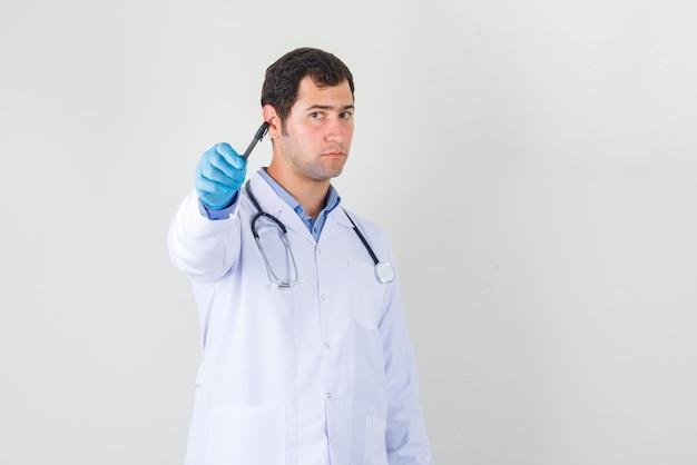 Male doctor pointing pen to the front in white coat, gloves front view.