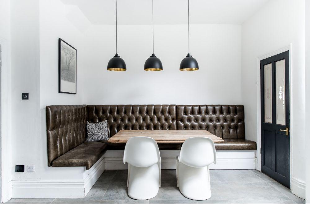 A stylish dining nook featuring a tufted leather banquette, rustic wooden table, sleek white chairs, and black pendant lights, showcasing a perfect blend of modern and classic commercial furniture design.