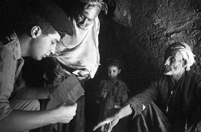 A l’intérieur d’un gourbi du camp de regroupement de Bordj Okhriss, un soldat français explique à des regroupés la réglementation en vigueur. Dans le secteur d’Aumale (à Sour El Ghozlane), en mai 1961.