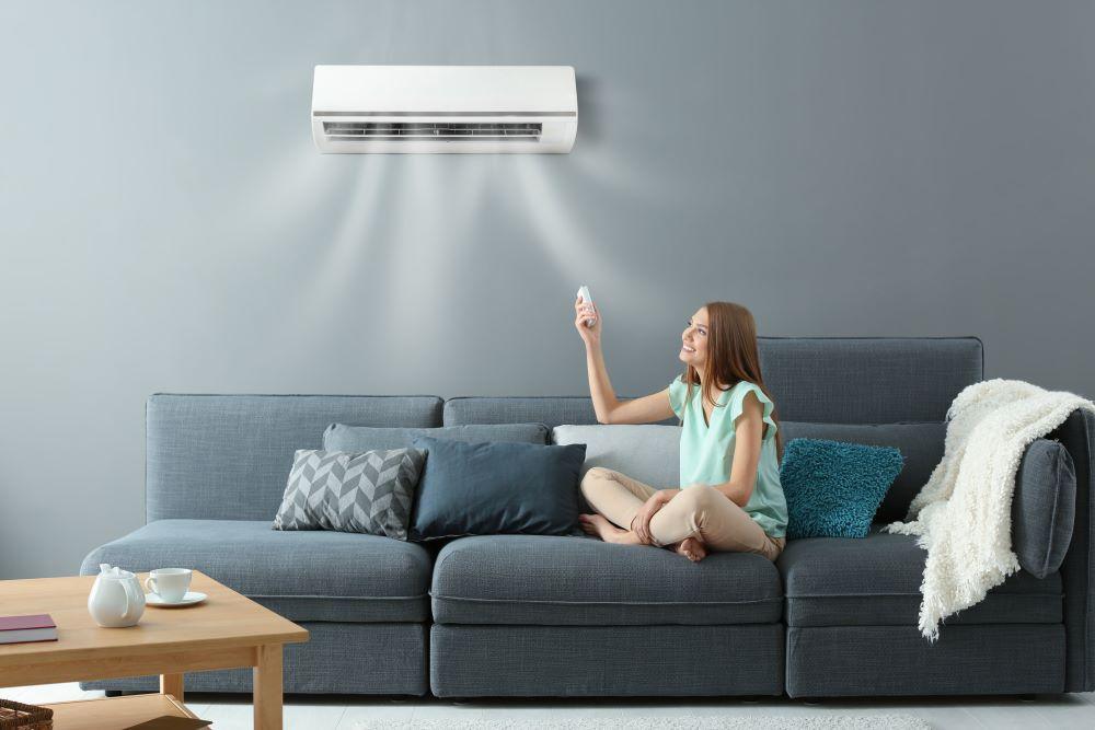 A woman sitting on a sofa holding an aircon remote, adjusting her Daikin air conditioner for perfect indoor comfort.