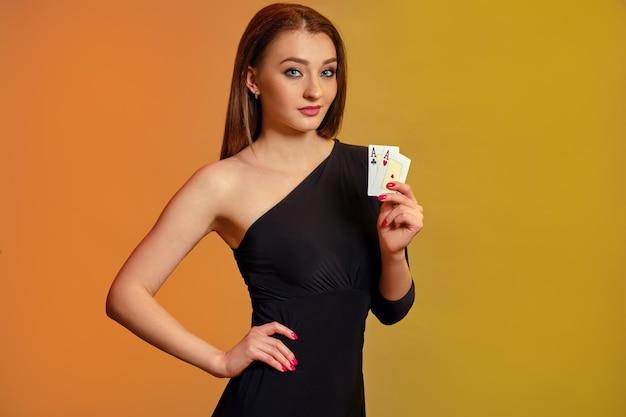 Photo blonde model with bright makeup in black dress is showing two aces posing against colorful backgroun