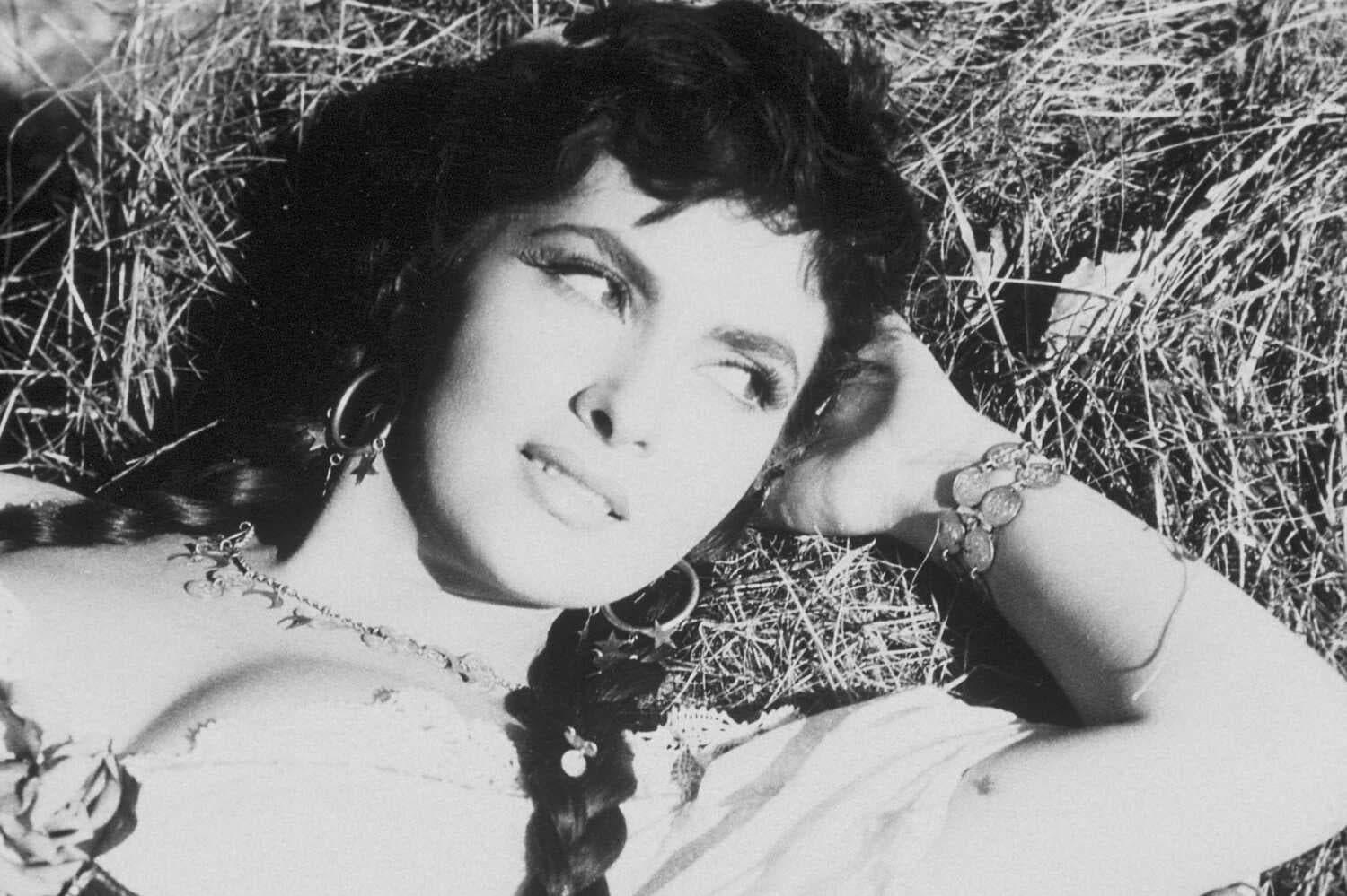 A young, dark-haired Gina Lollobrigida reclining on a haystack, her left hand behind her head.