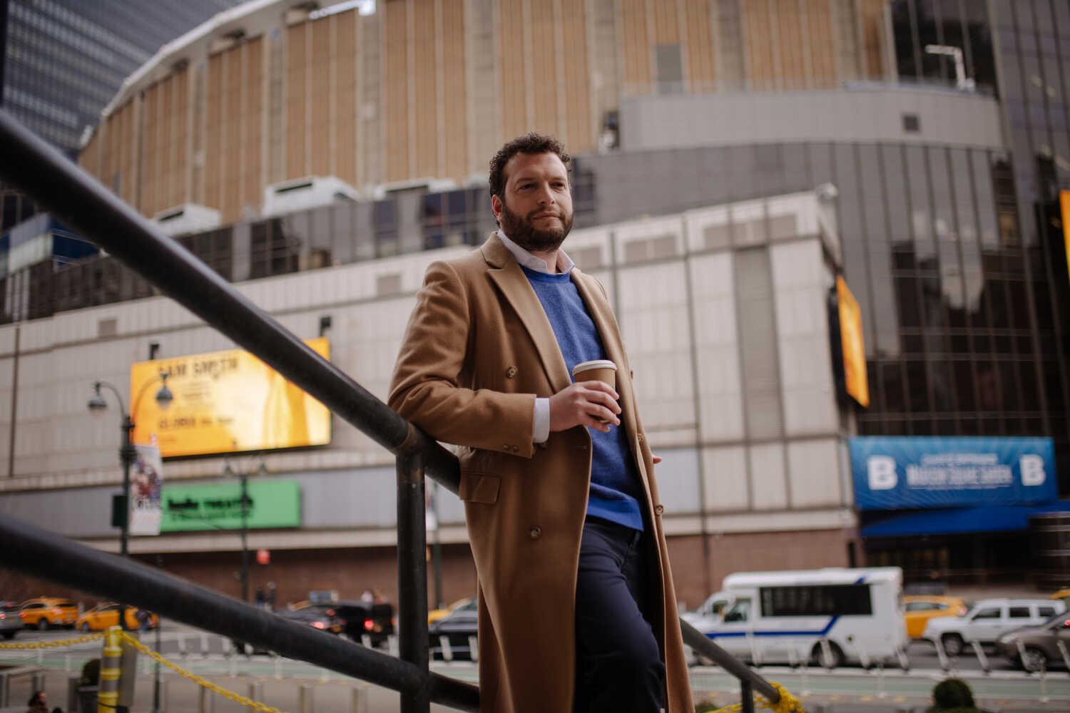 Benjamin Noren is standing on stairs in front of Madison Square Garden, leaning on a handrail, holding a coffee cup.