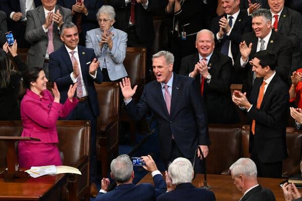 Kevin McCarthy, raising his hand, is surrounded by lawmakers on the House floor.
