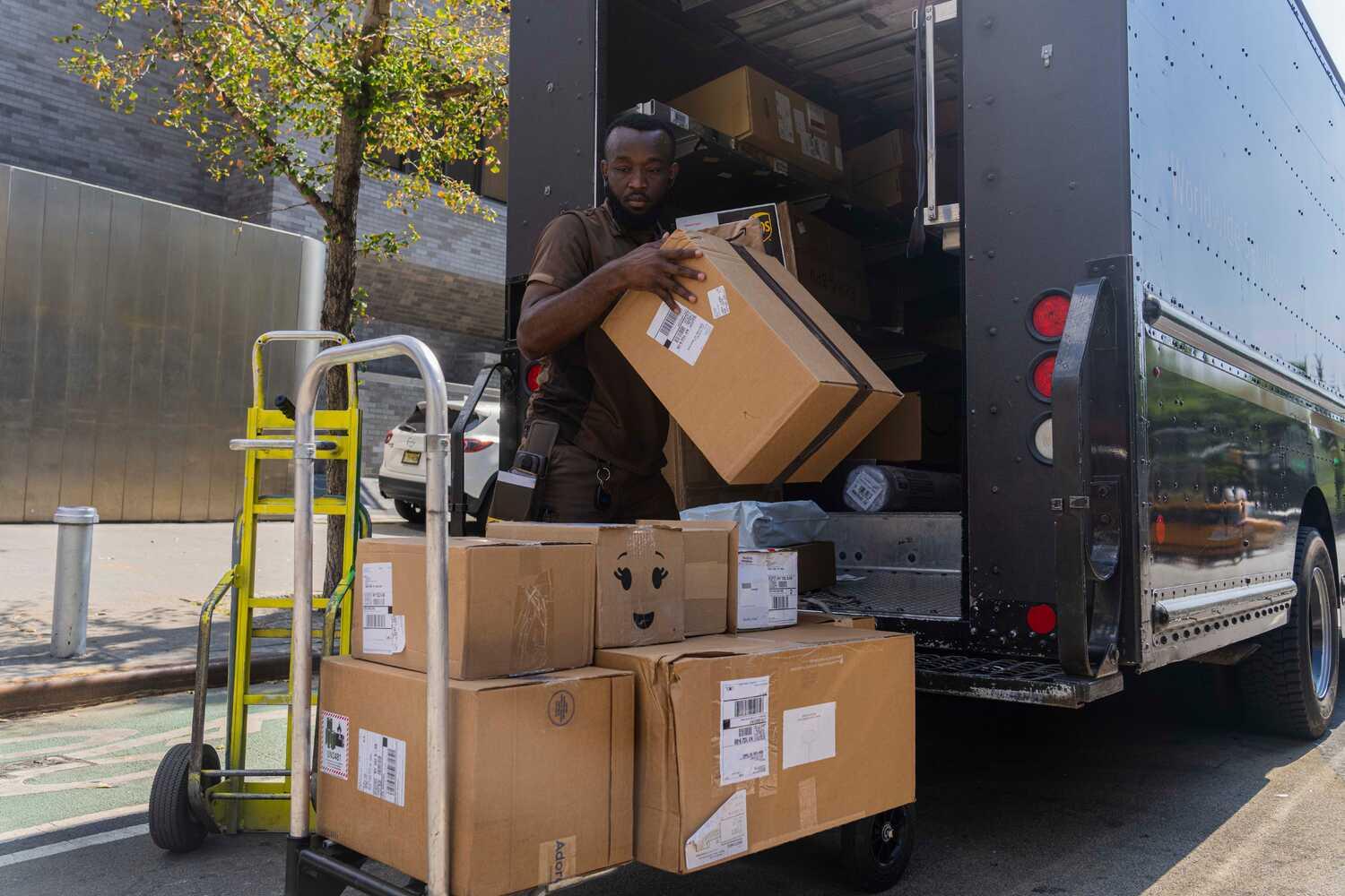 A Black man in a brown UPS uniform unloads packages from a truck on a Manhattan street.
