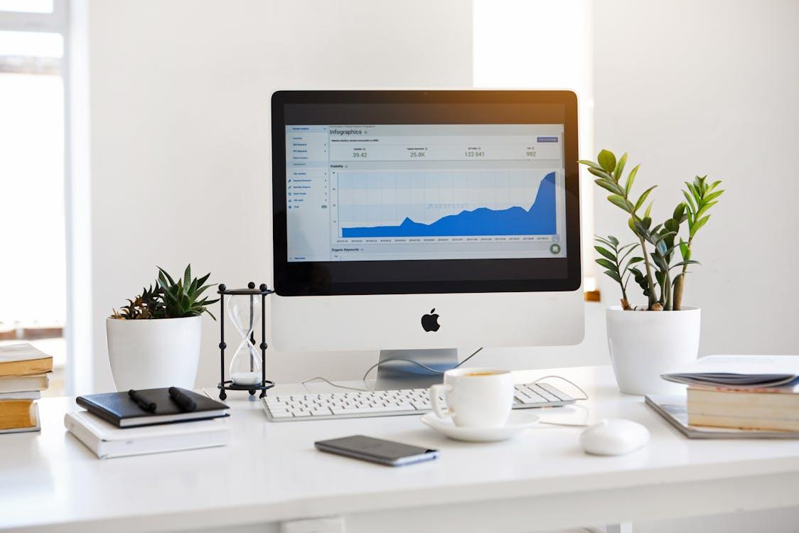 Free Silver Imac Displaying Line Graph Placed on Desk Stock Photo