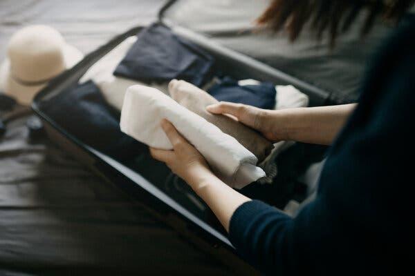 A woman is seen rolling some items to pack in a small suitcase.