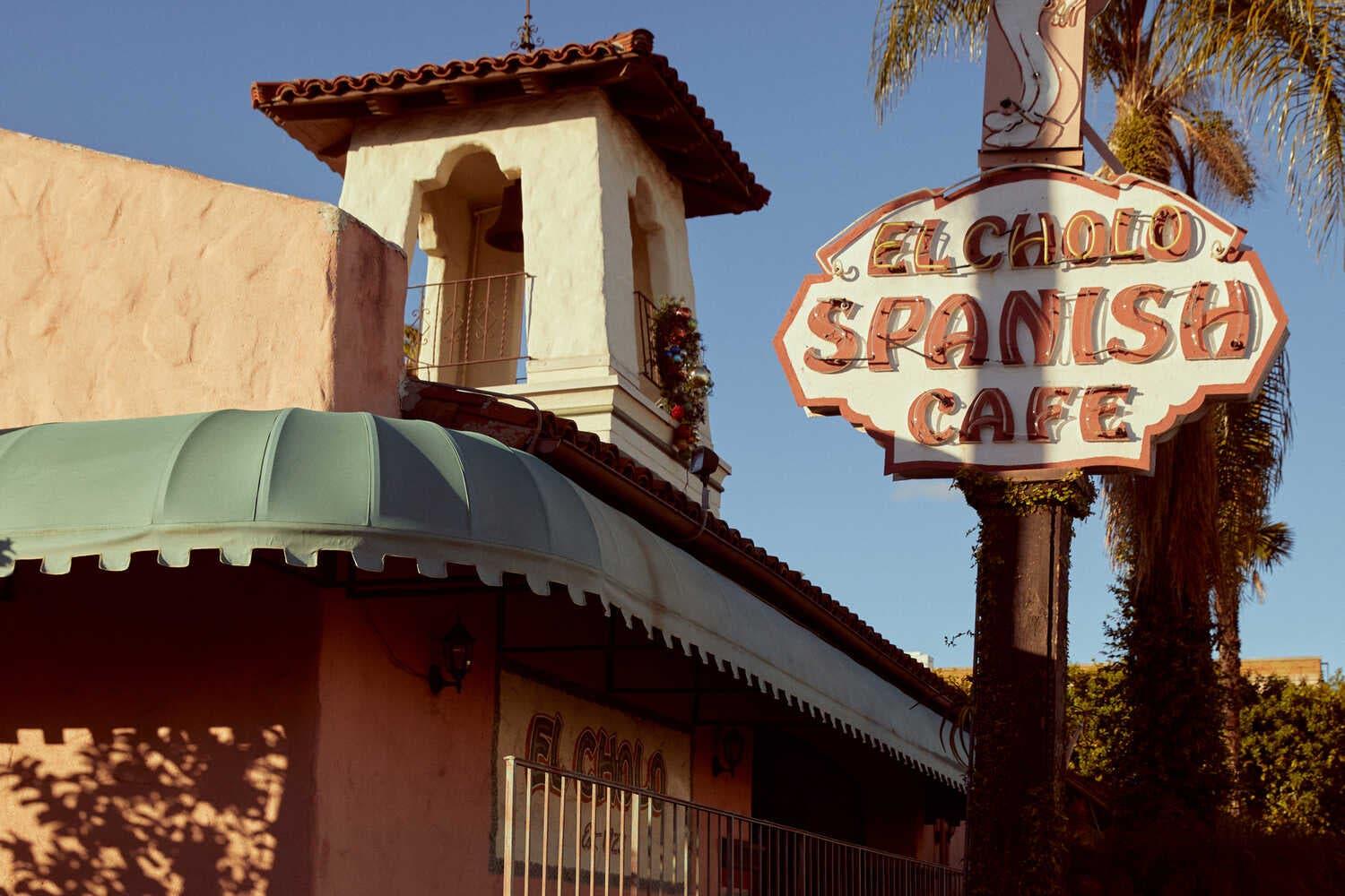 Two men stand under a sign reading “El Cholo Spanish Cafe.”