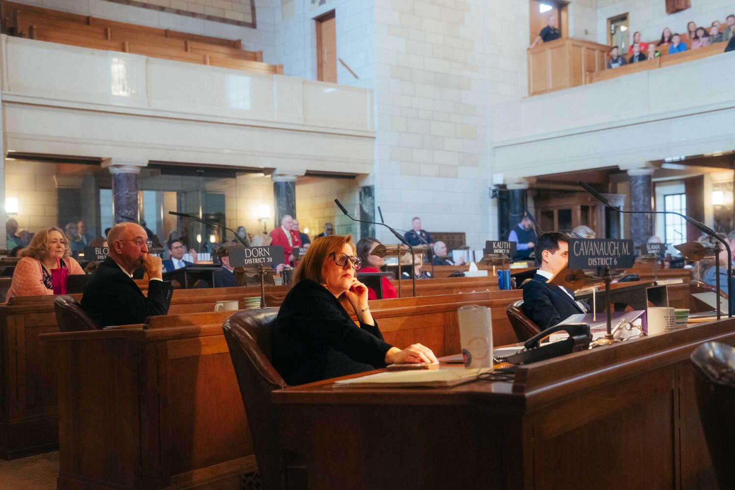 Senator Machaela Cavanaugh sits in the Nebraska state legislative chamber along with other lawmakers.