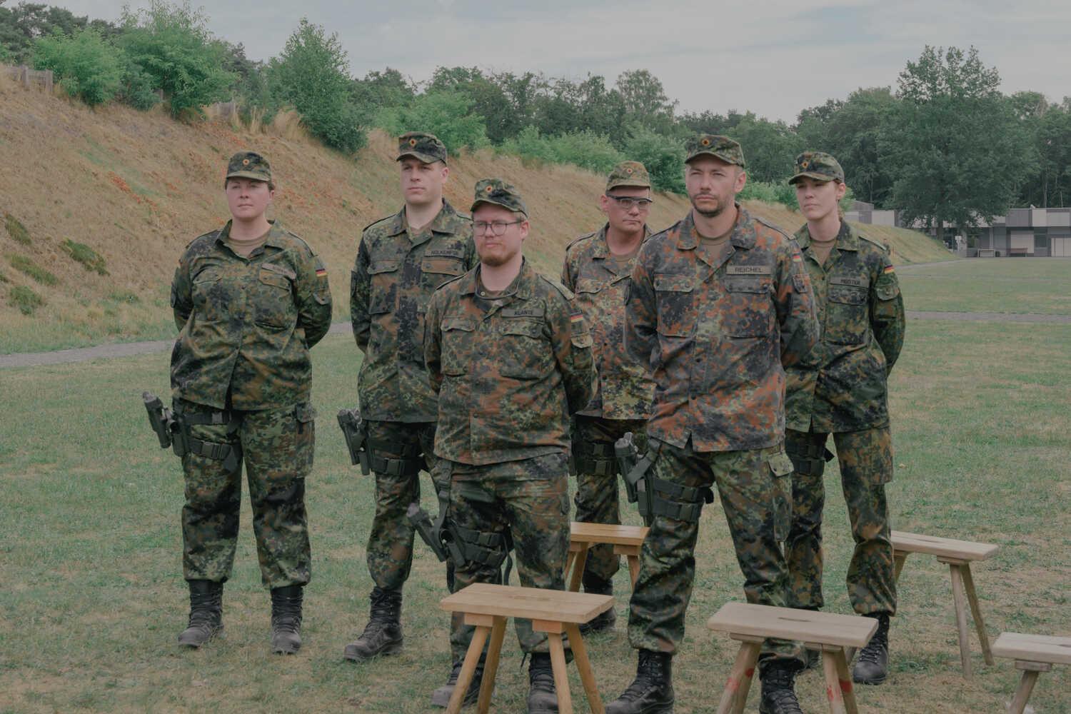 A photograph of six people in uniform standing with their arms behind their backs and looking forward.