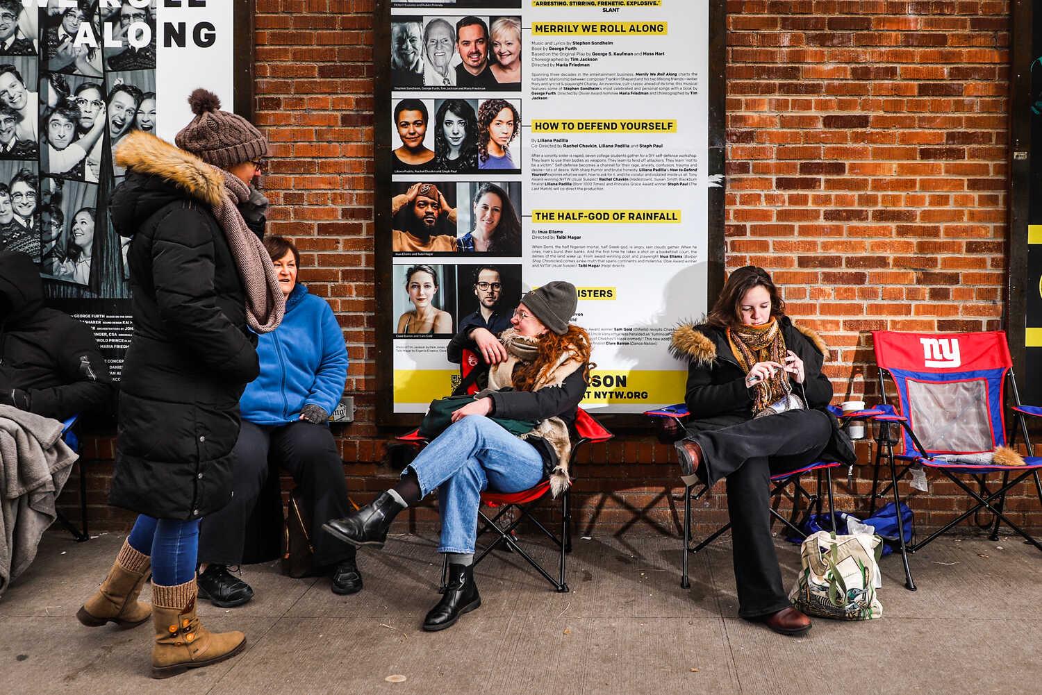 Women in winter coats wait outside a theater for last-minute tickets.