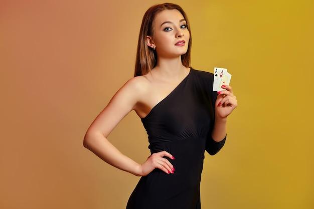 Photo blonde lady with bright makeup in black dress is showing two aces posing against colorful background