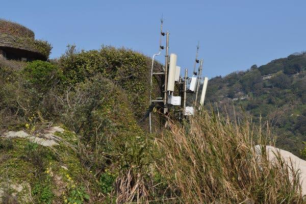 A mountain with grass and satellite equipment attached to a pole.