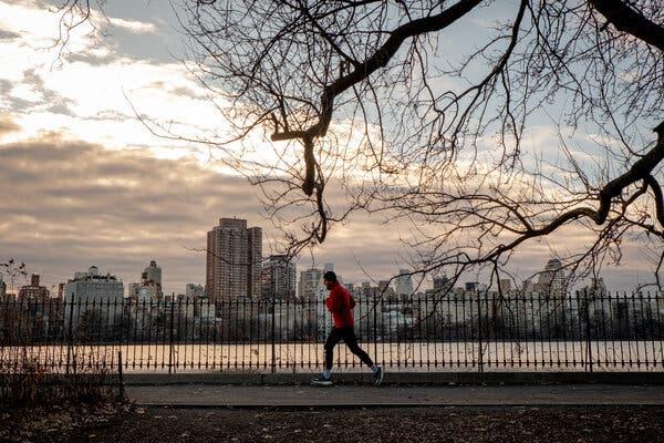 A wide shot of a jogger in the early morning with a cityscape behind him.