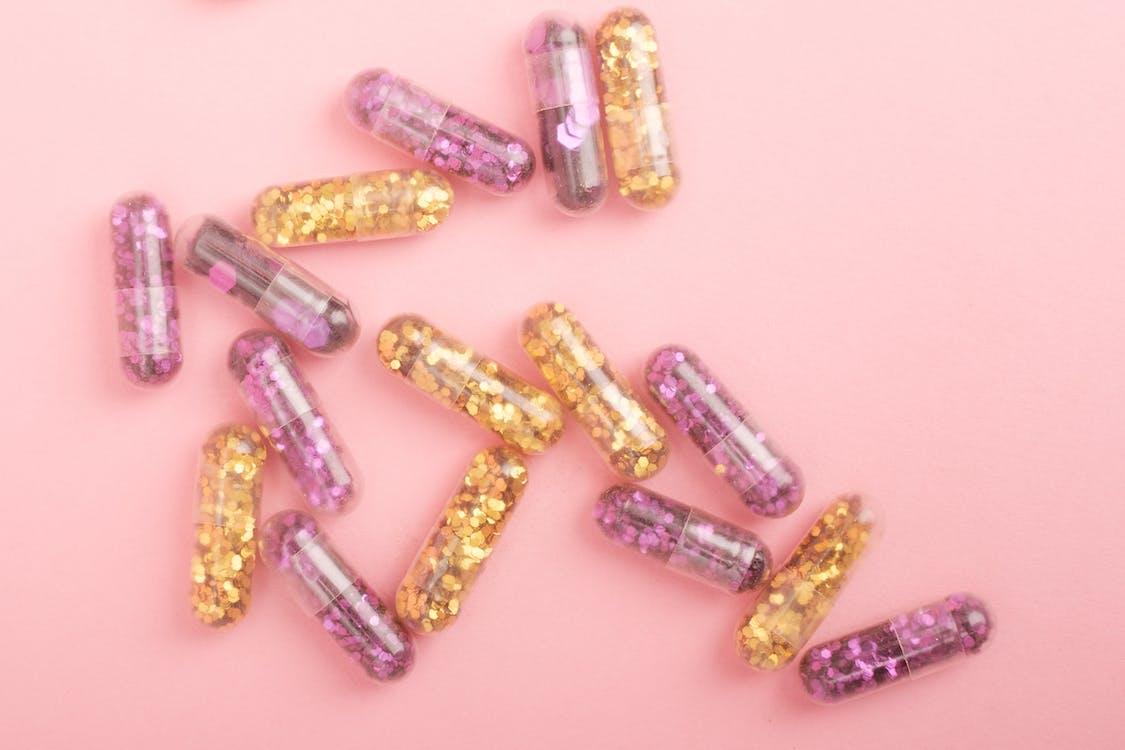 Free Pile of sparkling drug capsules scattered on pink surface Stock Photo