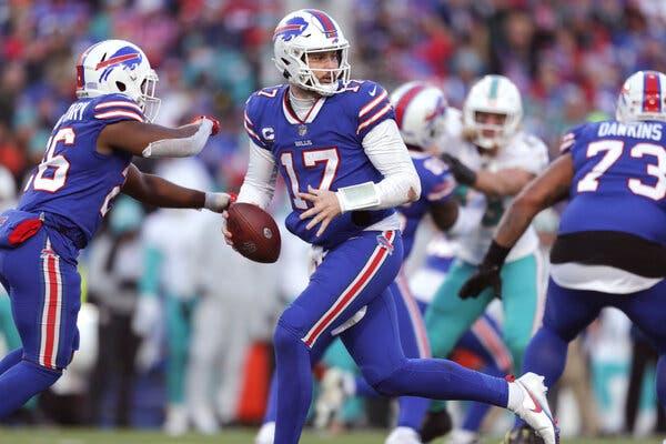 Bills quarterback Josh Allen, wearing No. 17 on his blue jersey, fakes the ball to the running back at his right while turning to his left.