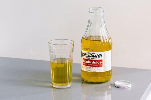 A glass of apple juice next to an open, partially emptied bottle of apple juice sitting on a gray countertop.