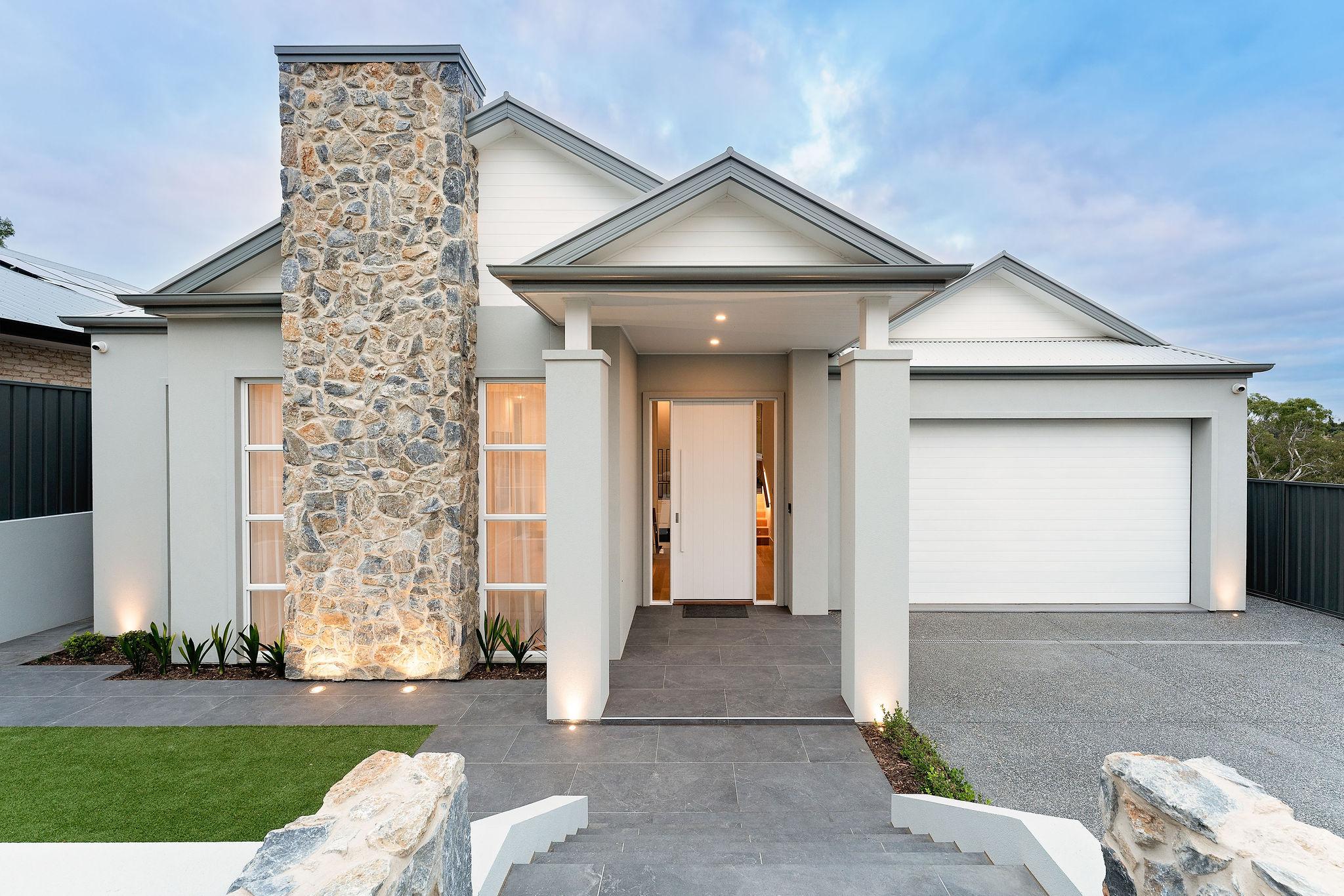 A modern house with a stylish stone pillar, sleek neutral walls, a grand entrance, and a spacious driveway leading to a double garage, showcasing knock down rebuild construction.