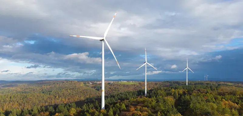 Drei Windkraftanlagen über einem farbenfrohen Herbstwald vor einem wolkigen Himmel, bei Schorndorf, Remstal, Rems-Murr-Kreis, Baden-Württemberg, Deutschland
