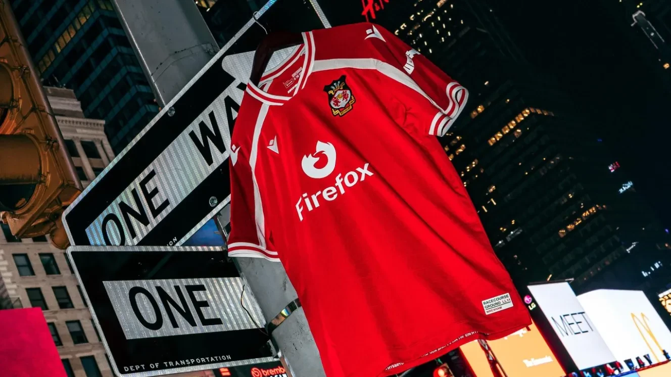 Wrexham AFC jersey hanging on a pole in Times Square, New York City, with "ONE WAY" signs and bright billboards in the background.
