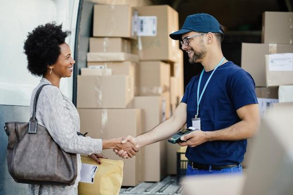 Happy courier handshaking with African American woman while delivering her a package