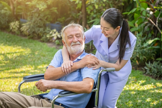 Free photo happy nurse holding elderly man hand on wheelchair in garden at nursing home