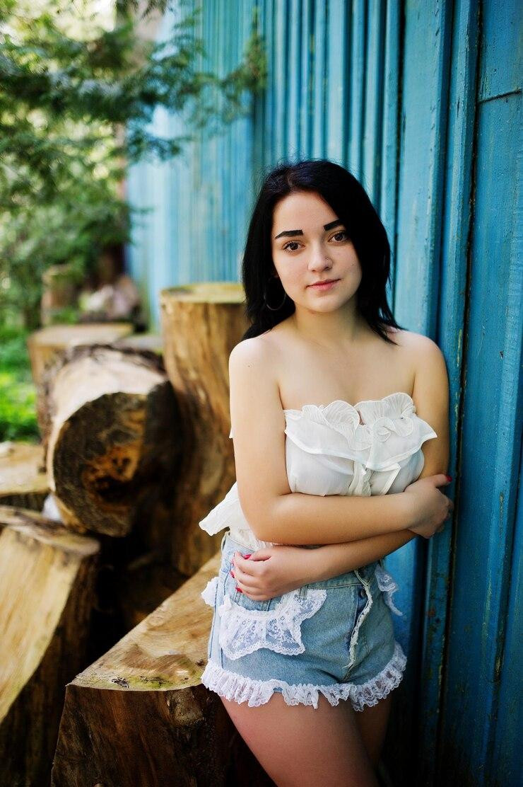 portraitsexybrunettegirlwomensjeansshortswhiteblouseagainstbluewoodenhousewithstumps_62782911859.jpg