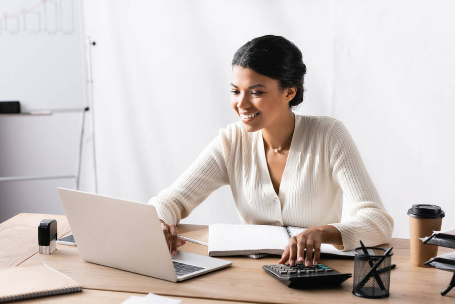 stockphotohappyafricanamericanwomanlookinglaptopwhileaccountingcalculatoroffice.jpg