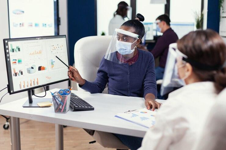 africanbusinesswomananalysingcolorfulgraphofficwearingfacemaskmultiethnicteamworkingcompanywithnewnormalrespectingsocialdistancebecauseglobalpandemicwithcoronavirus_4822579554.jpg