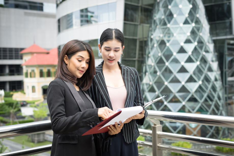 closeuptwobusinesswomanlookingwithpaperdocumenttogetherwhilewalkingofficebusinesspeopleconcept1.jpg