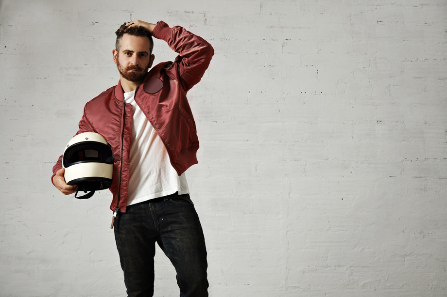 tiredyoungmotorbikerredbomberjacketblackjeanswhitetshirtadjustinghishairstyleholdinghiswhitehelmetmin.jpg